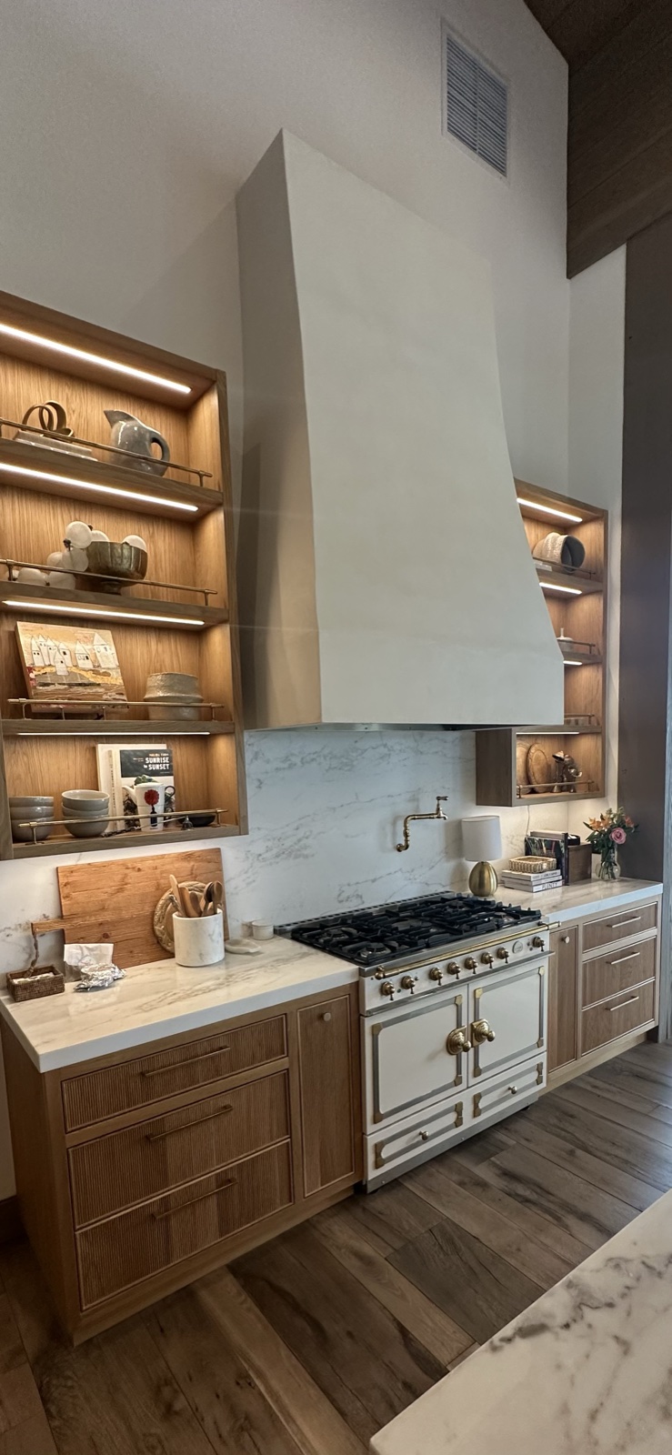Custom kitchen cabinetry with a plaster range hood, a professional range, and backlit display shelves in a San Diego home