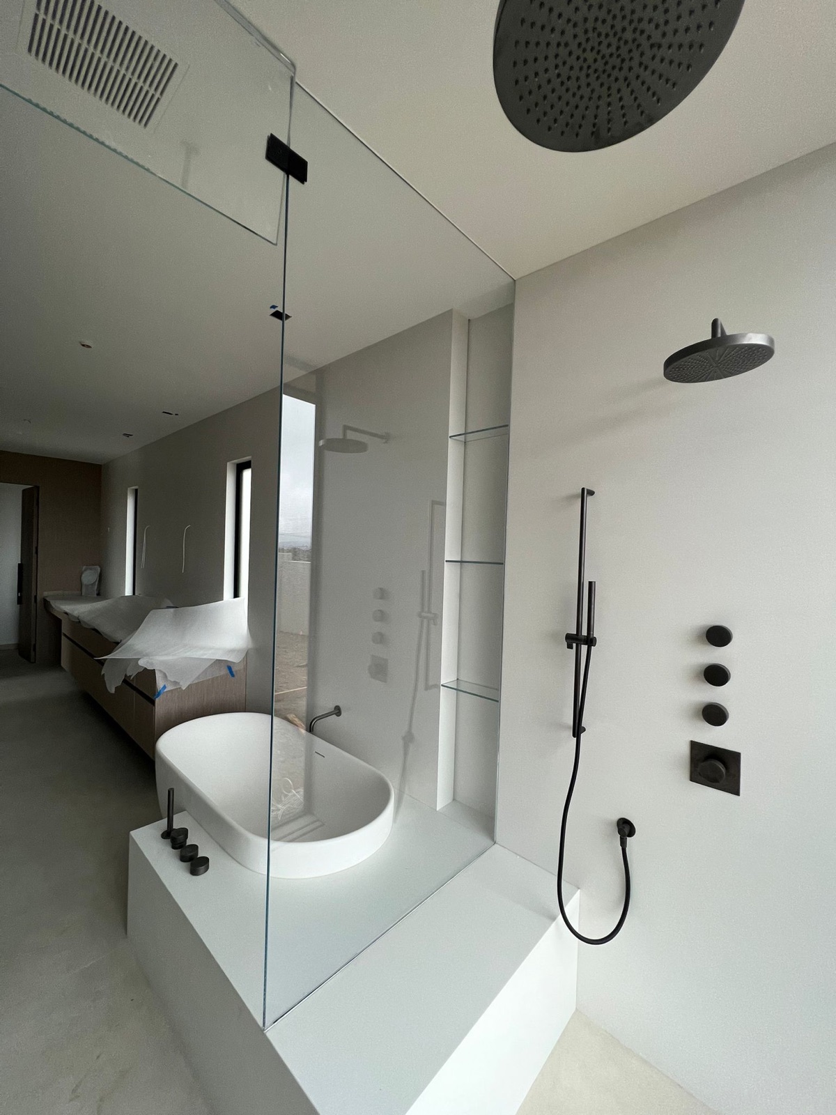 Frameless glass walk-in shower with a rain head and freestanding tub in a white marble bathroom, San Diego