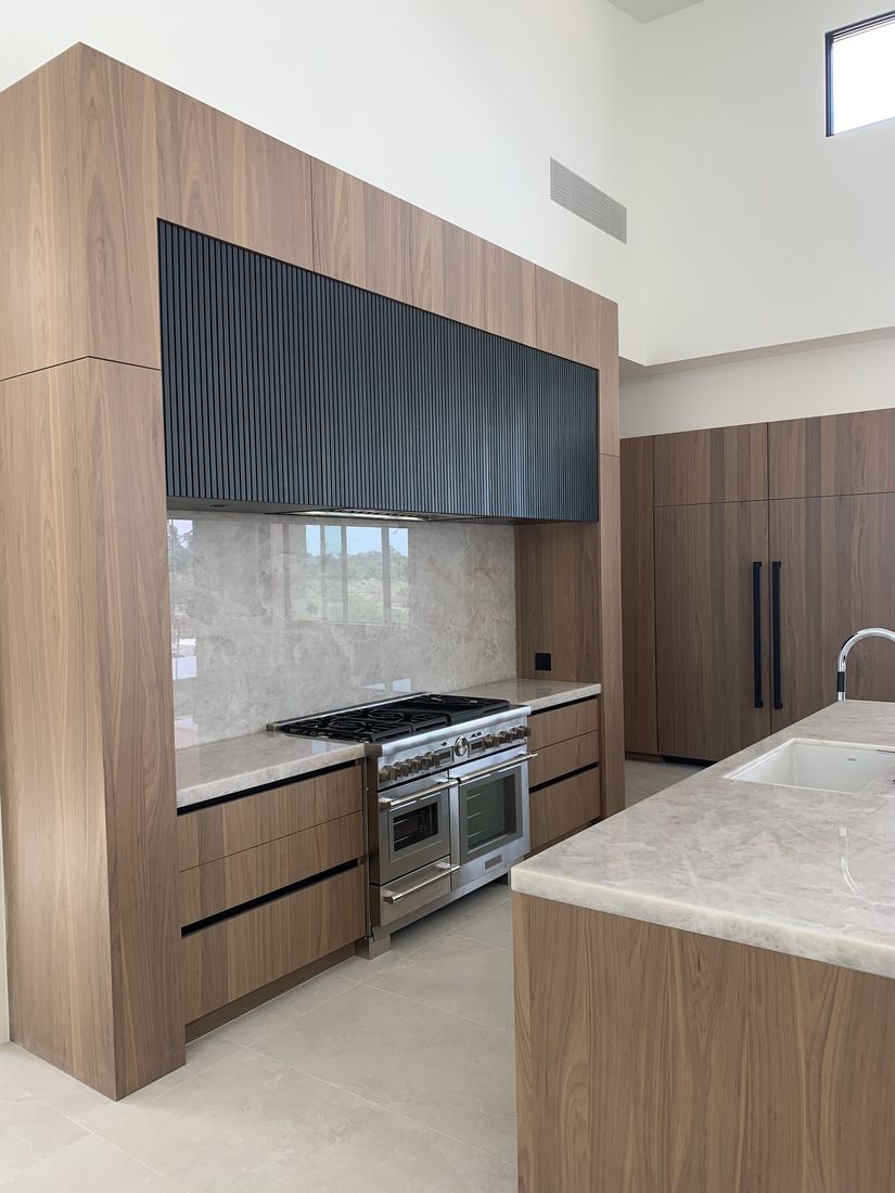 Custom kitchen with walnut fluted cabinetry, a pro range, and a stone backsplash, San Diego